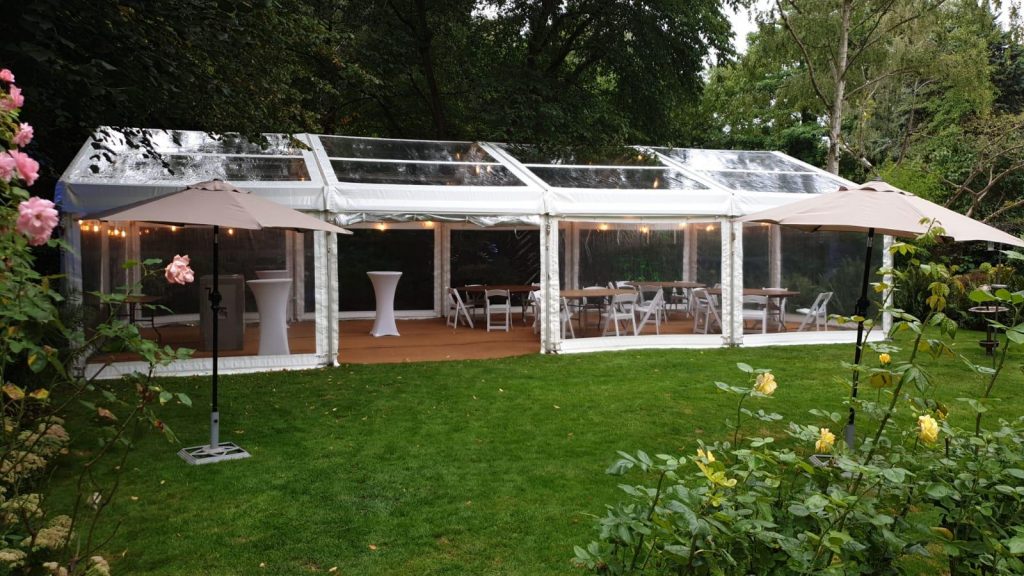 clear marquee in a garden for a summer party with coconut matting, tables and chairs